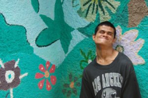 fotografía de un chico con parálisis cerebral frente a una pared con flores pintadas