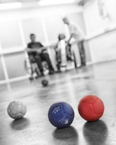 tres bolas de color. Al fondo personas en sillas de ruedas