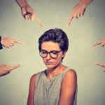 mujer con cara triste que es señalada por varias manos