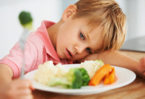 foto de un niño que mira fijamente un plato de comida con verduras