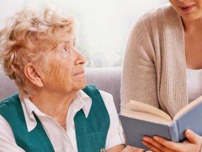 una mujer con alzheimer mira a otra que sostiene un libro